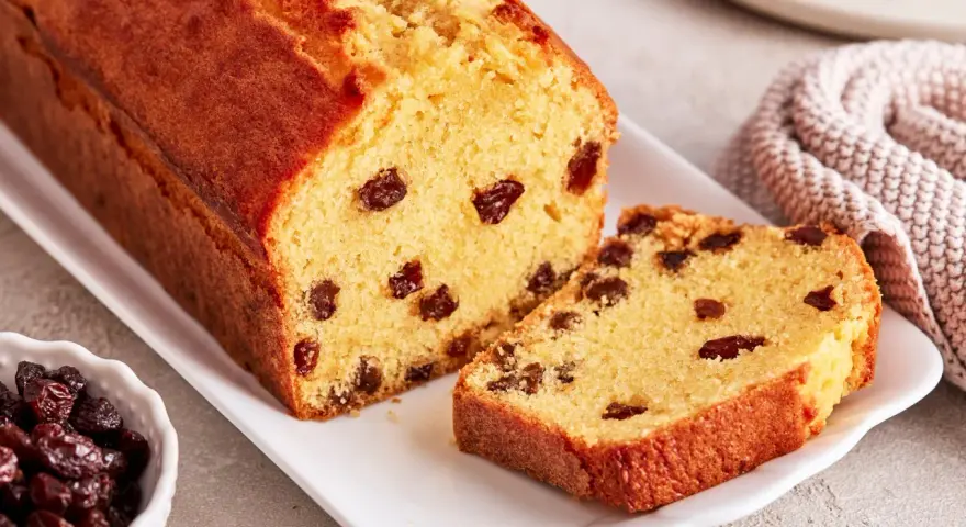 Ein saftiger Rosinenkuchen mit goldbrauner Kruste, auf einem weißen Teller angerichtet. Rosinen sind gut sichtbar im Teig verteilt.