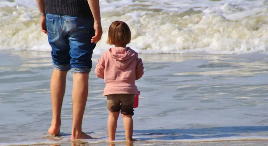 Ojciec i dziecko na plaży, cieszący się wspólnym urlopem ojcowskim 9 tygodni.