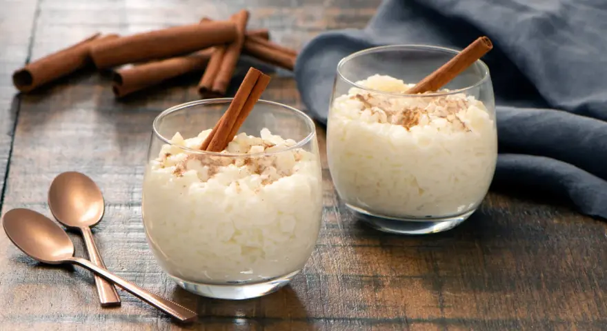 Dos copas de cremoso arroz con leche, espolvoreado con canela y decorado con una rama de canela.