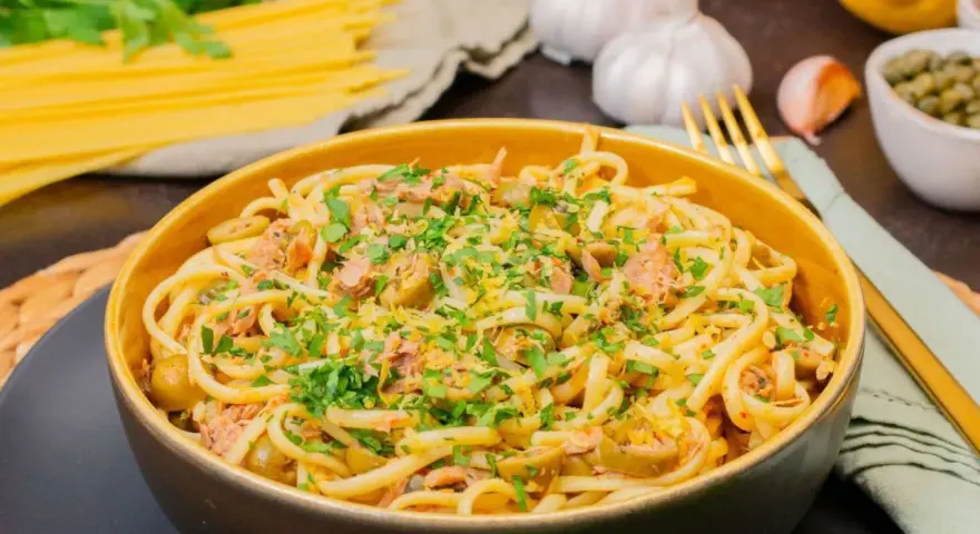 Eine Schüssel mit Thunfisch Pasta, garniert mit Petersilie und Zitronenschale. Oliven und Kapern sind ebenfalls sichtbar.