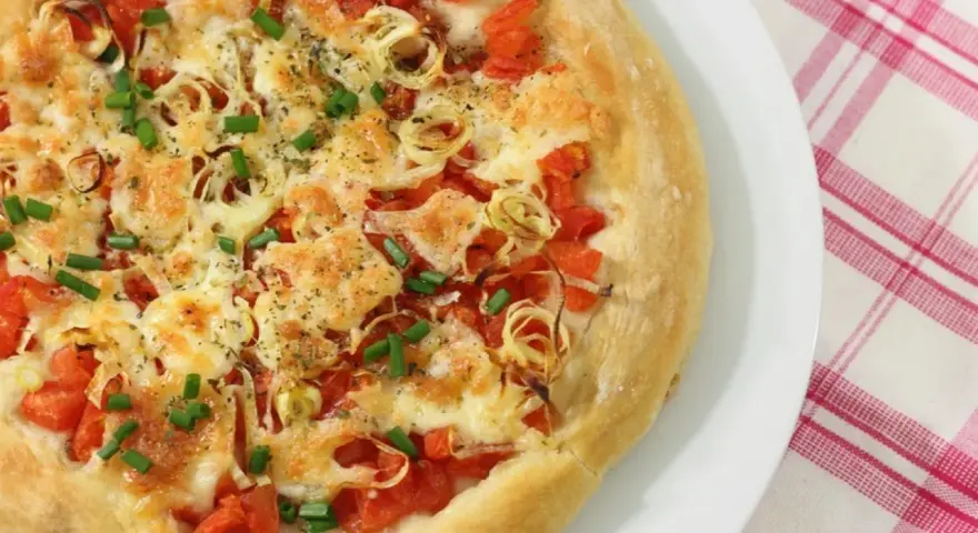 Pizza casera con tomates, queso derretido, cebolla y cebollino. Los ingredientes de esta pizza casera lucen deliciosos.