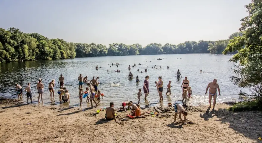 Menschen genießen einen sonnigen Tag im Strandbad Hamburg. Kinder spielen im Sand, während Erwachsene im Wasser planschen.
