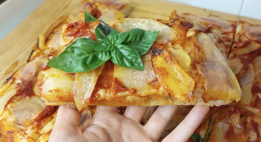 Una fetta di pizza di patate dorata, guarnita con basilico fresco, pronta per essere gustata.