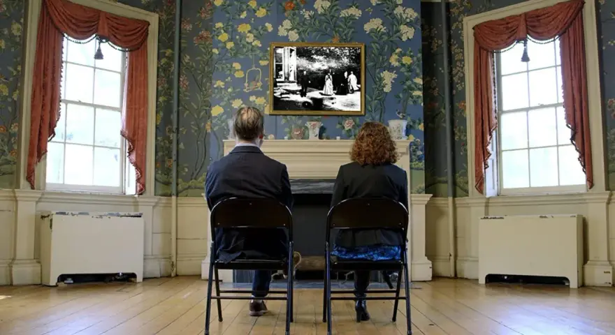 Coppia seduta di spalle, guarda un quadro con una scena di giardino, "Roundhay Garden Scene", su una parete fiorita.