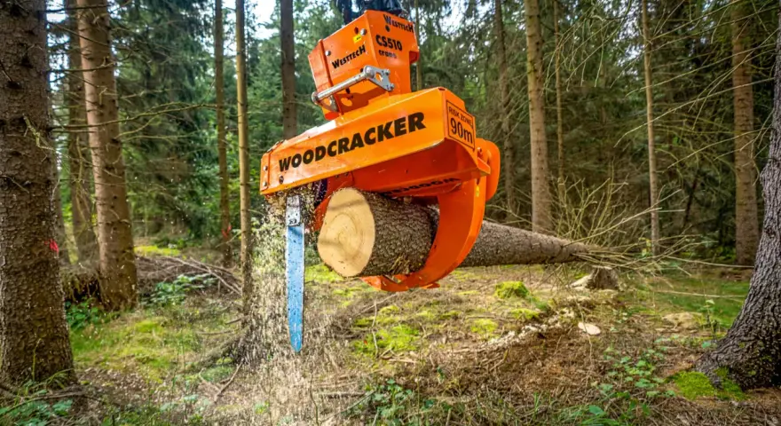 Pomarańczowe maszyny leśne do zrywki drewna, model Woodcracker, tną pień drzewa w lesie.