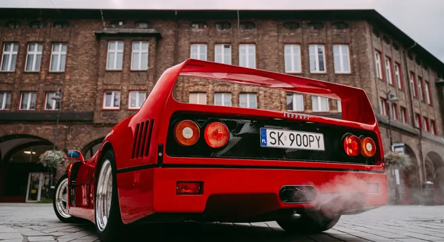 Czerwone Ferrari F40 z dymem z wydechu na tle ceglanego budynku.