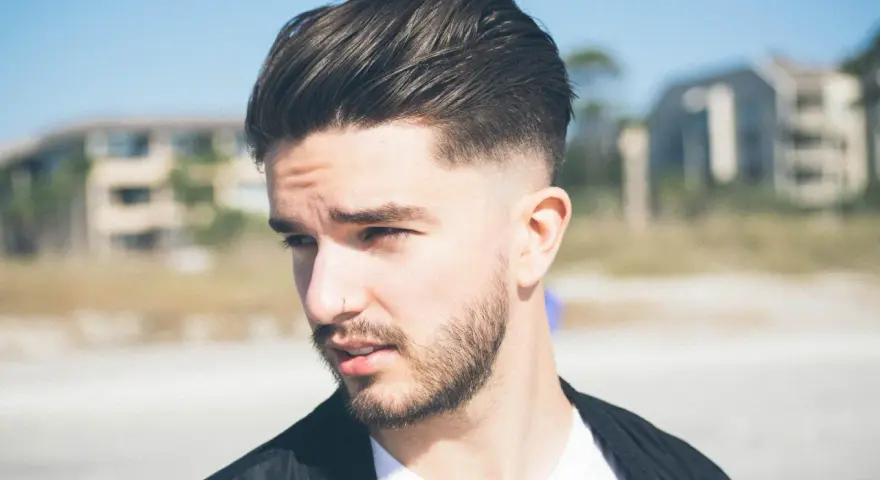Joven con barba y cortes de pelo hombre elegante, peinado hacia atrás con degradado.