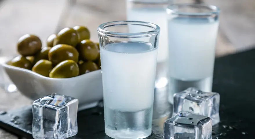 Raki, ein Getränk, das oft mit Griechenland assoziiert wird, wird aus Trauben hergestellt. Hier sind Gläser mit Raki, Eiswürfel und Oliven.