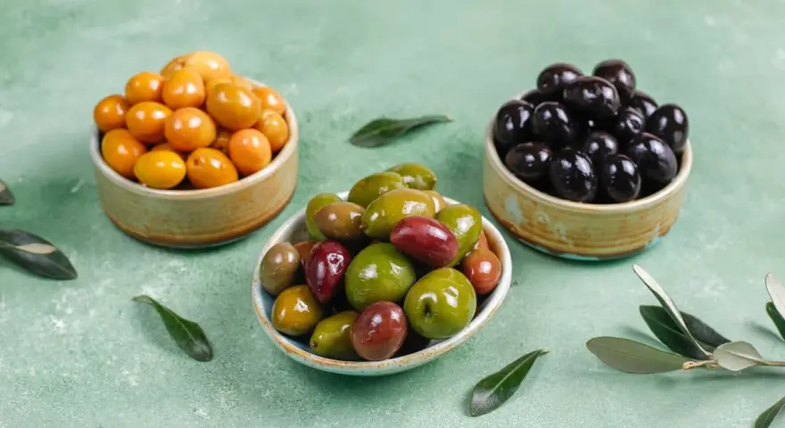 Tres cuencos con aceitunas de diferentes colores: amarillas, verdes y negras.