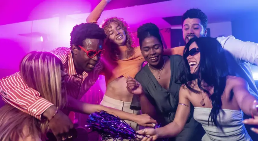 Fröhliche Freunde tanzen ausgelassen zu ihrer **dance music playlist** im Club, umgeben von lila und blauer Beleuchtung.
