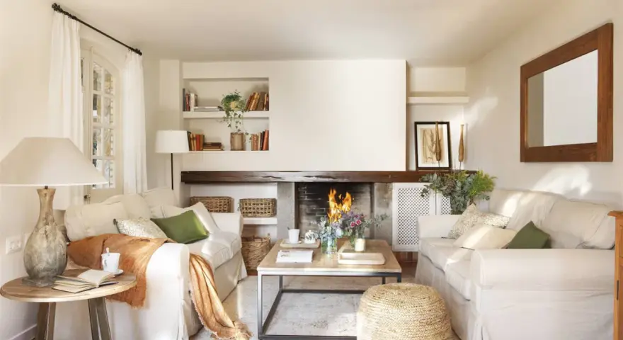 Salón acogedor con chimenea encendida, sofás blancos, mesa de centro de madera y detalles decorativos.