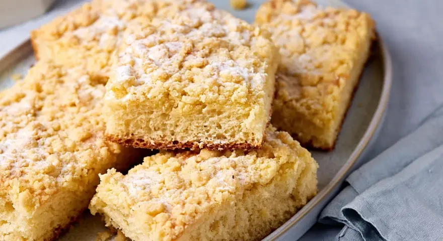 Saftiger Streuselkuchen vom Blech, mit Puderzucker bestäubt, auf einem Teller angerichtet.