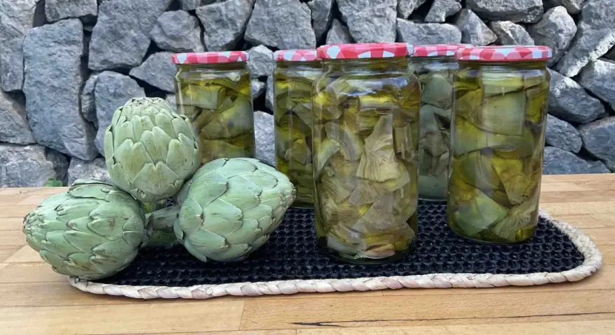 Alcachofas frescas y en conserva en frascos, sobre una mesa de madera y fondo de piedra.