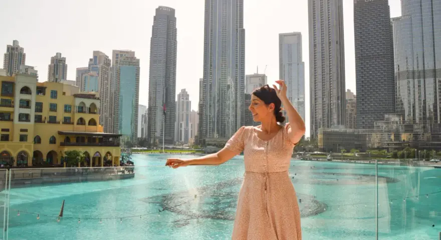 Mujer disfrutando de su viaje a Dubai, con rascacielos y una fuente de agua de fondo.