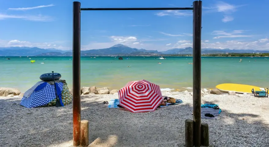 Słoneczne plaże nad Jeziorem Garda, z turkusową wodą, górami w tle i kolorowymi parasolami.