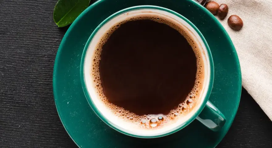 Aromatic coffee in a green cup, next to chocolate and beans. Czy kawa podnosi kortyzol? This morning brew might be the answer.