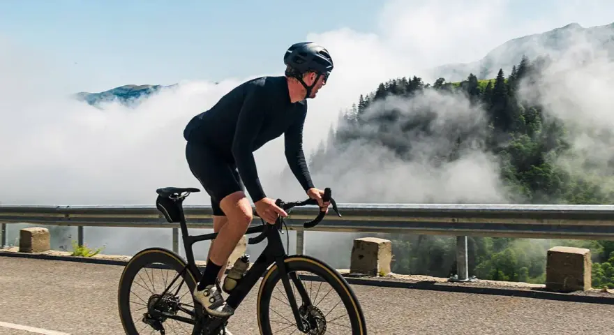 A cyclist in black gear conquers a mountain road, enjoying the breathtaking views and the freedom of long rides amidst swirling clouds.