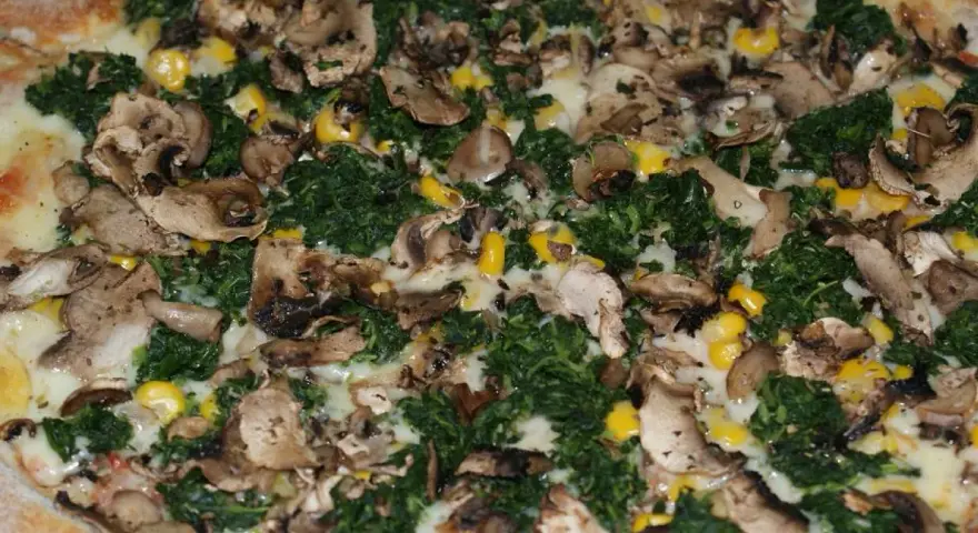 Pyszna pizza ze szpinakiem, grzybami i kukurydzą, obficie posypana serem.