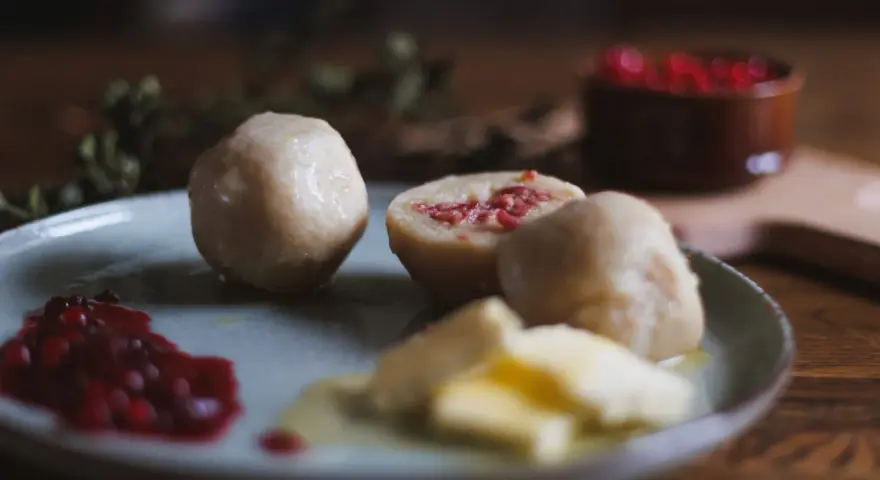 En tallrik med pitepalt, lingonsylt och smör. En halv palt visar en fyllning av fläsk. Perfekt för ett recept på pitepalt.