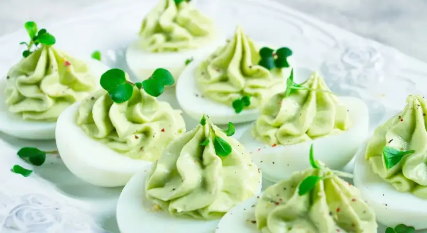 Uova ripiene pasquali, guarnite con crema verde e germogli freschi, pronte per essere gustate.