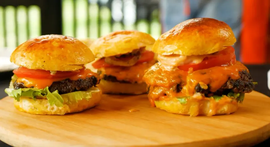 Trzy soczyste burgery z roztopionym serem, pomidorem i sałatą na desce.