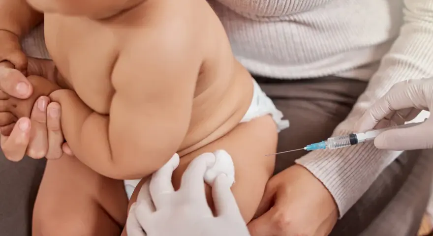 Dziecko otrzymuje szczepienie. Ręka w rękawiczce trzyma strzykawkę, a druga ręka przygotowuje miejsce wkłucia. To ważny moment dla zdrowia, jak w przypadku szczepionki heine medina.