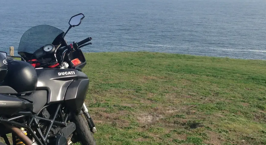 Motocykl Ducati zaparkowany na trawie z widokiem na morze. Marzenie o podróży przez Szwecję motocyklem.