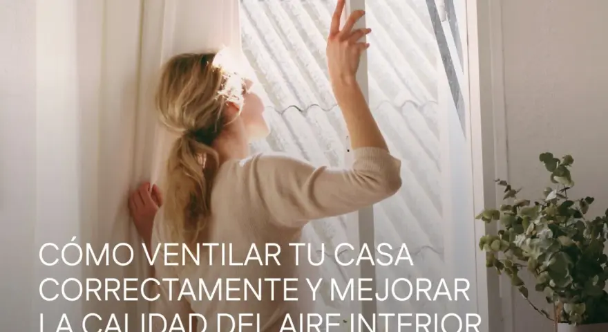 Mujer abriendo ventana para mejorar la **calidad del aire interior**. La luz del sol ilumina su cabello rubio recogido.