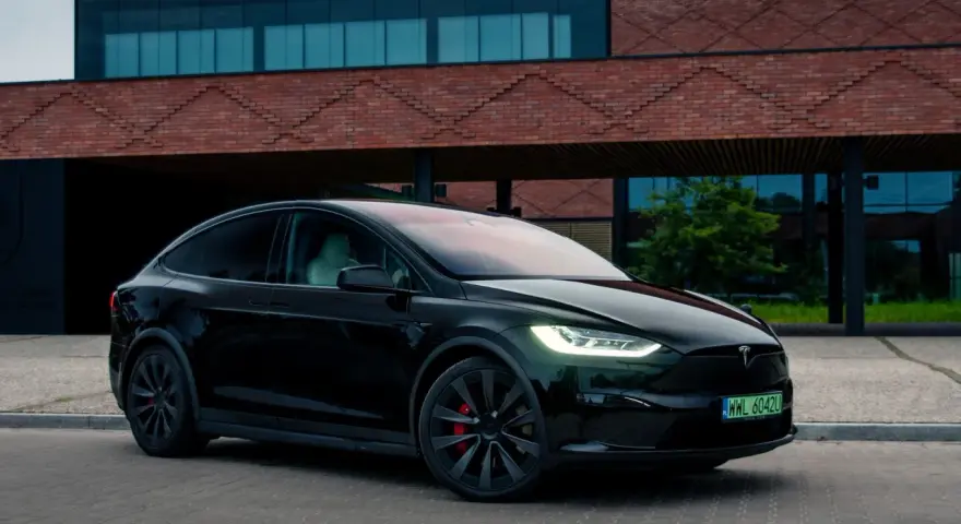Czarny Tesla Model X zaparkowany przed nowoczesnym budynkiem z cegły.