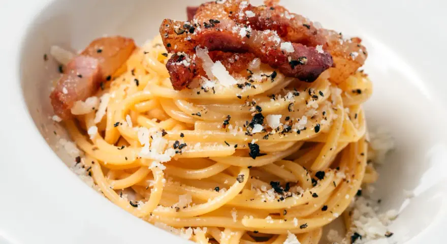 Spaghetti carbonara z chrupiącym guanciale, posypane parmezanem i czarnym pieprzem. To właśnie guanciale nadaje autentyczny smak.