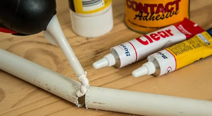 Klej w tubce i pistolet do klejenia na drewnianym blacie. Zastanawiasz się, czym usunąć klej super glue z mebli?
