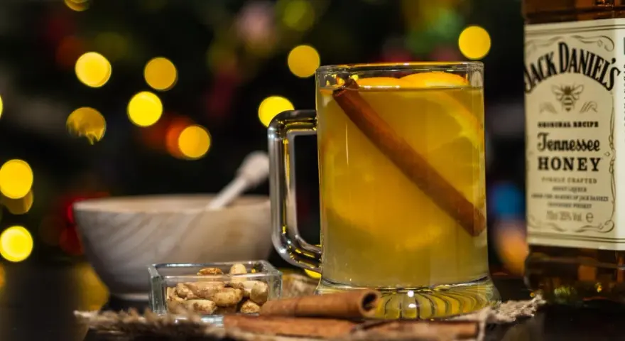 Rozgrzewający drink z Jack Daniels Tennessee Honey, z pomarańczą i cynamonem, w blasku świątecznych światełek.