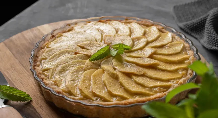 Tarta de manzana casera, con láminas de manzana doradas y una hoja de menta fresca en el centro.