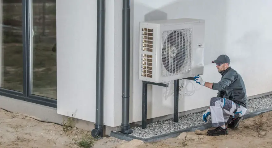 Instalator sprawdza pompę ciepła 3 fazową zamontowaną na ścianie budynku.