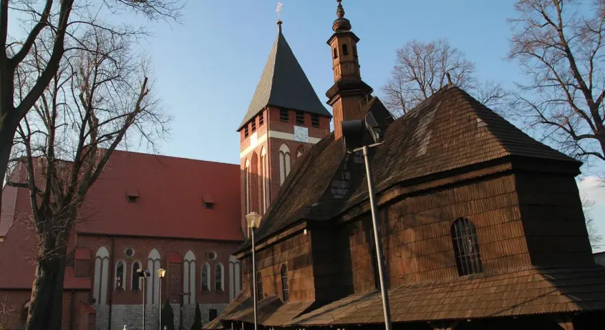 Drewniana i ceglana architektura kościołów w miasteczku śląskim, z wieżą zegarową i strzelistymi dachami, pod błękitnym niebem.