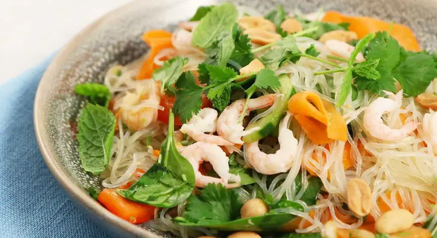En läcker asiatisk nudelsallad med räkor, morötter, gurka, jordnötter och färska örter.