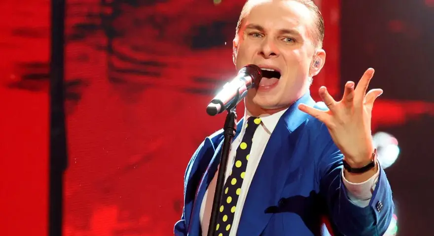 Artysta w niebieskiej marynarce i krawacie w grochy śpiewa do mikrofonu. To jego piosenka do góry, pełna energii.