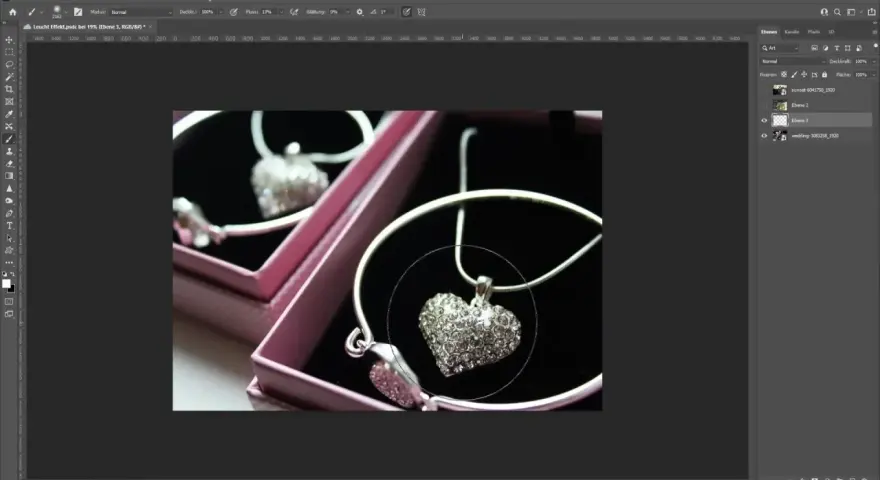 Un collier en forme de cœur orné de strass, dans une boîte rose. Un effet lumière Photoshop est appliqué pour le faire scintiller.