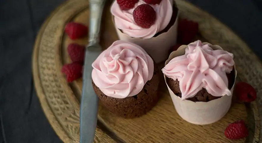 Tre chokladcupcakes med rosa frosting och hallon, redo att avnjutas. Ett perfekt cupcakes recept för alla tillfällen.