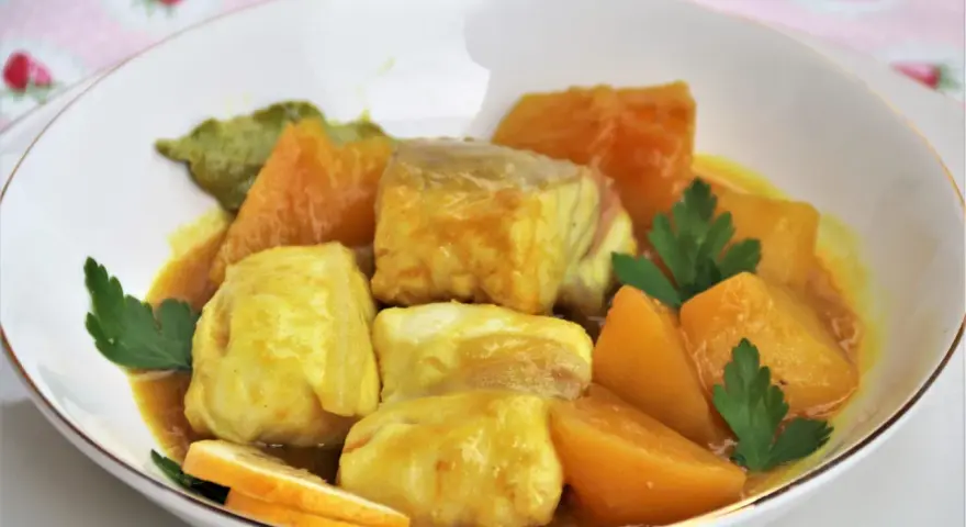Sabroso cazon en amarillo, con trozos de pescado blanco y patatas en una salsa dorada, decorado con perejil y rodajas de limón.