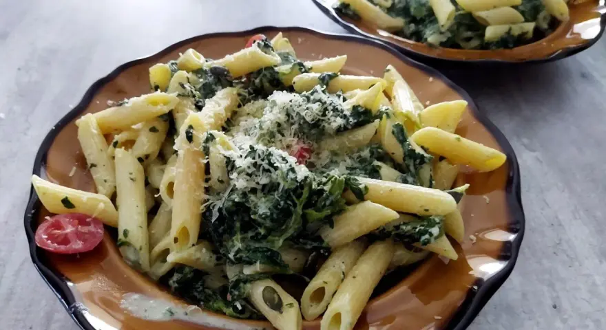 Penne z fetą i szpinakiem, posypane parmezanem. Prosty przepis na makaron ze szpinakiem i fetą.
