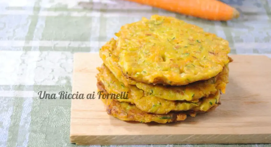 Pancakes dorati di frittata con farina di ceci, serviti su un tagliere di legno, con carote sullo sfondo.