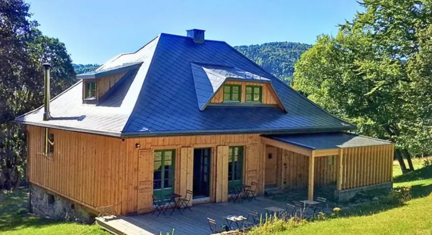 Drewniany domek z niebieskim dachem, tarasem i zielonymi okiennicami. Idealne schronisko oźna na górskim stoku.