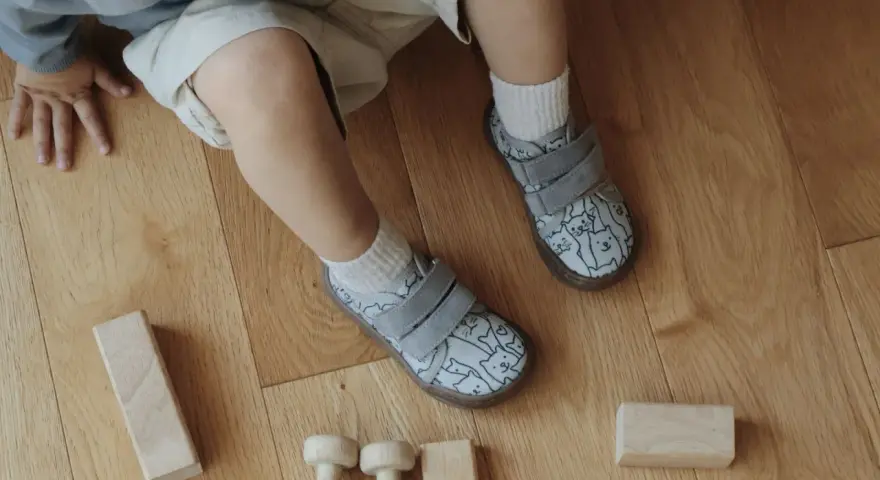 Roczne dziecko bawi się klockami na drewnianej podłodze. Ma na sobie buty z kotkami, idealne do chodzenia po domu.