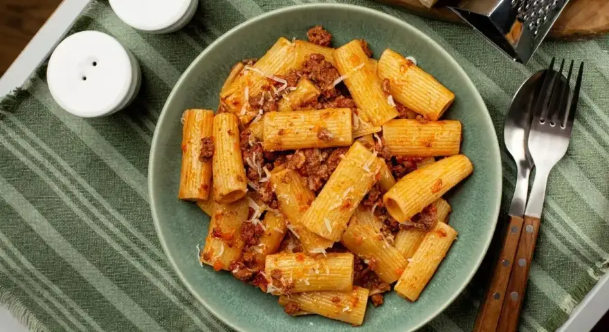 Pyszne makaron grube rurki z sosem bolońskim i parmezanem, gotowe do jedzenia.
