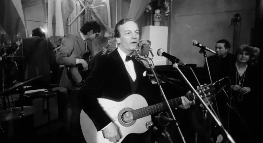 Zbigniew Kurtycz z gitarą i zespołem wykonuje swoje utwory. Wokalista w czarnym aksamitnym fraku śpiewa do mikrofonu.