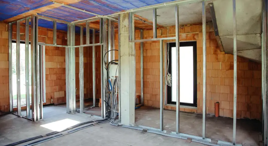 Konstrukcja pod scianke dzialowa z plyty kartonowo gipsowej, widoczne profile metalowe, instalacje elektryczne i hydrauliczne, sciany z cegly.