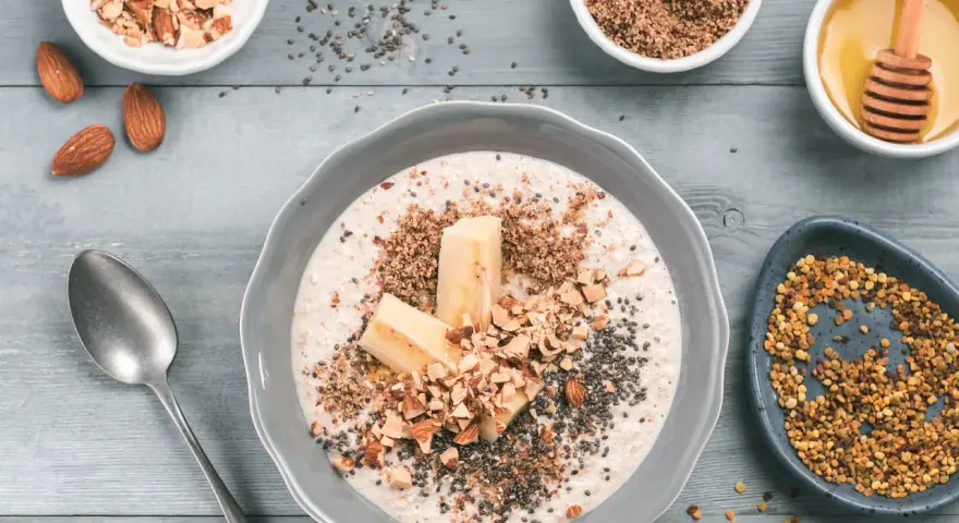 Avena con plátano, almendras picadas, chía y miel, rodeada de ingredientes.
