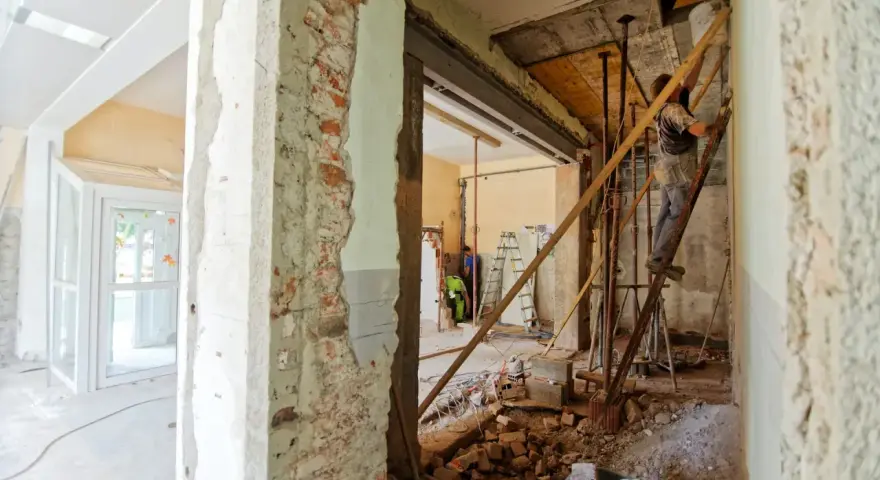 Trwa remont domu. Widać rozbiórkę ścian, gruz i pracowników na drabinach.