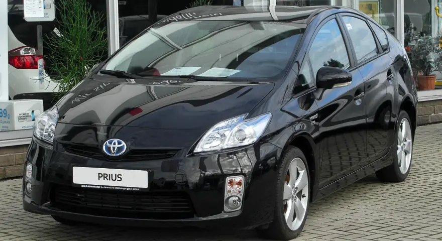 Czarny Toyota Prius 3, hybrydowy samochód, lśni na tle salonu samochodowego.